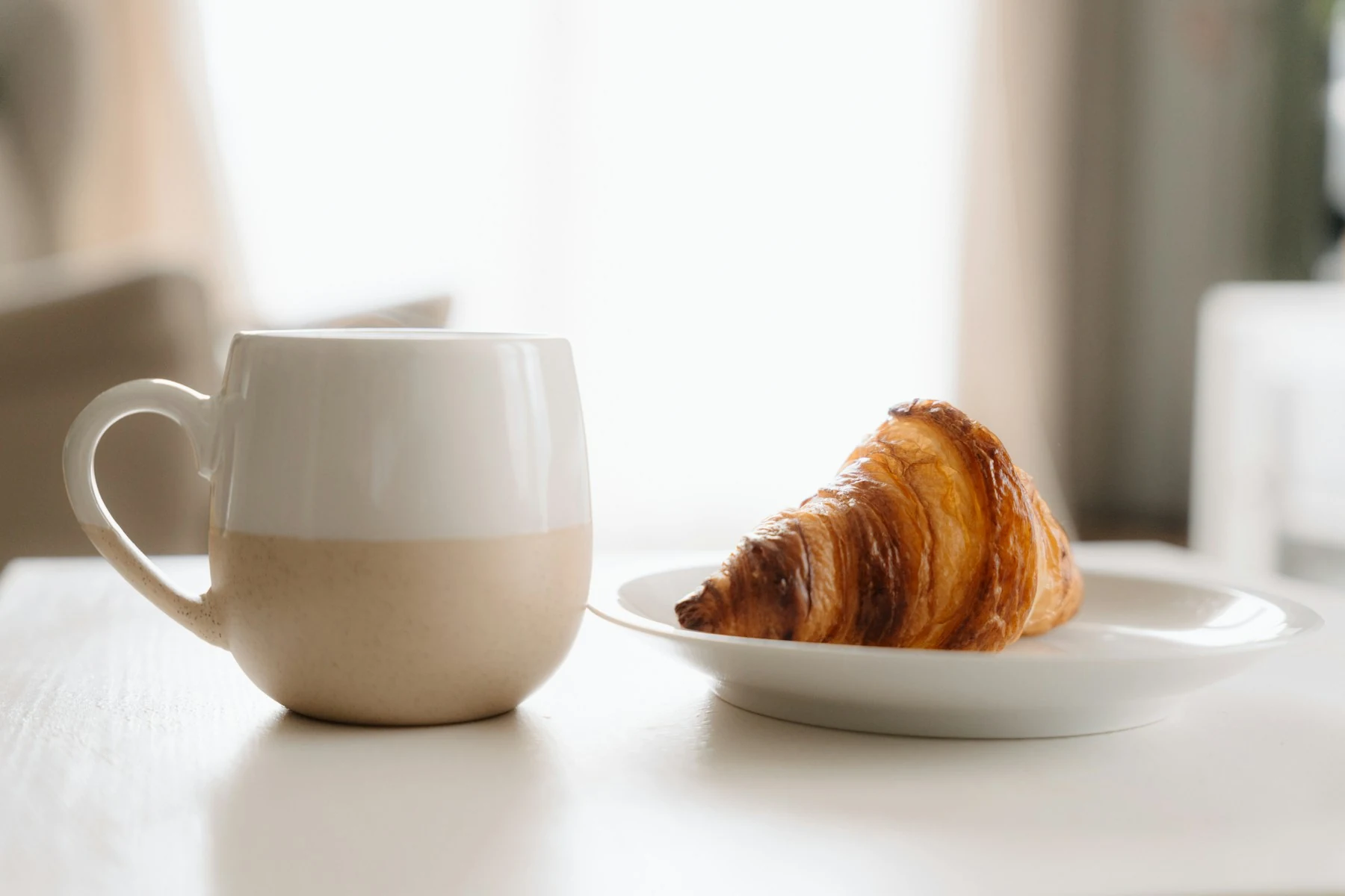 白いテーブルに置かれたクロワッサンとコーヒーカップ
